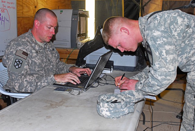 Sgt. Philip Smith, a Camarillo, Calif., native and a financial management support team noncommissioned officer in-charge with Charlie Detachment, 24th Finance Company, types up financial information as a Soldier fills out paperwork to receive cash...
