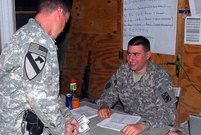 Spc. Blaine Berquist, a Puyallup, Wash., native and a cashier with Charlie Detachment, 24th Finance Company, gives cash to a Soldier during a trip to Joint Security Station McHenry in Kirkuk province, Iraq, Dec. 4. Berquist is part of a team of...