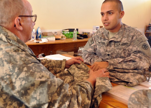 Spc. Agapito Reyes, a 263rd Quartermaster Company shower, laundry, and clothing repair specialist and Sanelizario, Texas, native, discusses what repairs need to be done on a uniform with a customer here Jan. 8. (U.S. Army photo by Sgt. Matthew C. Coo...