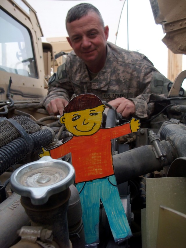 CONTINGENCY OPERATING LOCATION Q-WEST, Iraq - Staff Sgt. Stephen S. Poff, a squad leader from Ashland, Miss., inspects the engine of his gun truck at Contingency Operating Location Q-West Jan. 13 with "Flat Stanley," a paper doll used in a pen-pal...