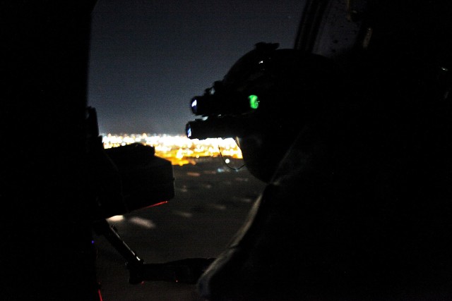 CAMP TAJI, Iraq - Through the green light of night vision goggles, Command Sgt. Maj. Glen Vela, from Dallas, the command sergeant major for 1st Air Cavalry Brigade, U.S. Division - Center, scans the airspace around a UH-60 Black hawk helicopter durin...