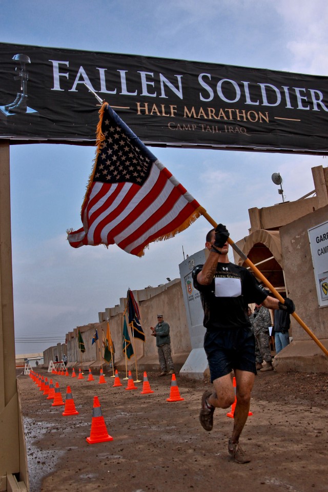 CAMP TAJI, Iraq - In grand style, Senior Airman Matthew Klundt, from Fresno, Calif., of 732nd Expeditionary Security Forces Squad, carries an American flag as he crosses the finish line to claim first place in the Fallen Soldier Half-Marathon run...