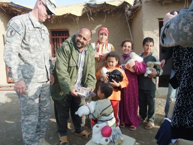 CONTINGENCY OPERATING LOCATION Q-WEST, Iraq -Capt. Drew Clark (left), a resident of Madison, Miss., looks on as Khalil Abrahim hands his son Muhammed a plastic bag of pencils and crayons, at his farm near Al Qayarrah, during a security escort mission...