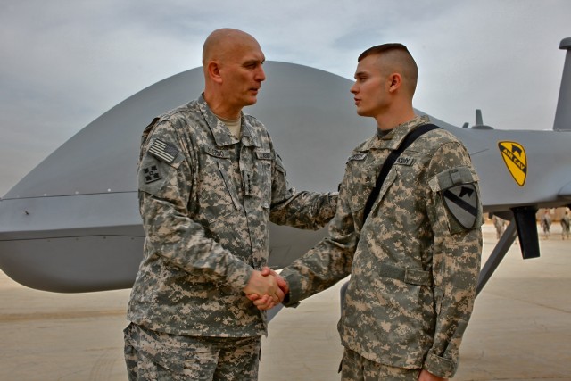 CAMP TAJI, Iraq - An MQ-1C Sky Warrior unmanned aerial vehicle provides an imposing backdrop, as Gen. Ray Odierno, from Rockaway, N.J., commanding general, U.S. Forces-Iraq, presents Sgt. Justin Palowitch, from Grayson, Ky., a UAV operator, Quick Rea...