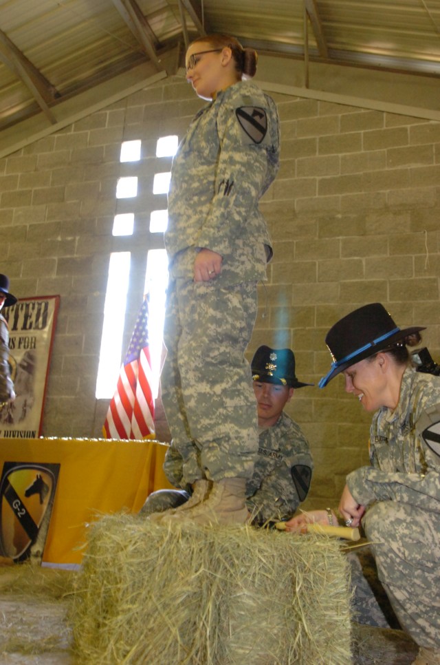 FORT HOOD, Texas - Pfc. Elizabeth Stanton (left), a Topeka, Kan. native, mounts a hay bale as Master Sgt. Sheila Bounds, a Raleigh, N.C. native, hammers on her newly earned 'Combat Spurs', March 25, at Belton Lake Recreational Area. ...
