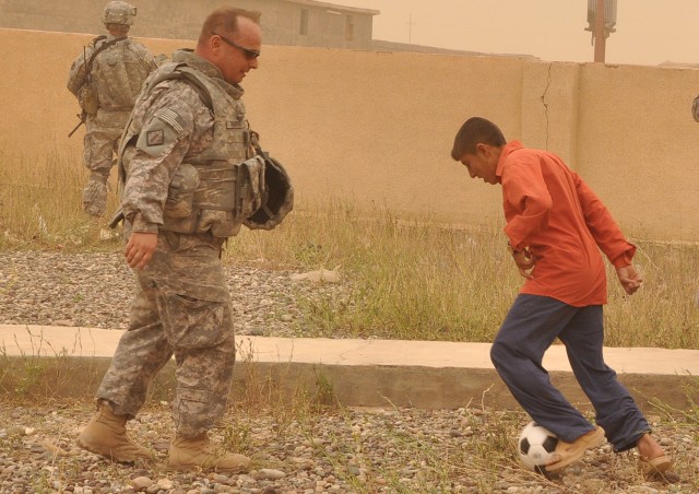 Maj. Scott Wadyko, a Jacksonville, Fla., native and 15th Sustainment Brigade, 13th Sustainment Command (Expeditionary), deputy operations officer, plays soccer with a local Iraqi boy during a visit to the school here April, 12. (U.S. Army photo by...