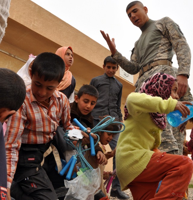 Chavo, the native Iraqi interpreter for 15th Sustainment Brigade, 13th Sustainment Command (Expeditionary), talks to local children while they take gifts from the unit during a visit to the school here April 12. (U.S. Army photo by Staff Sgt....