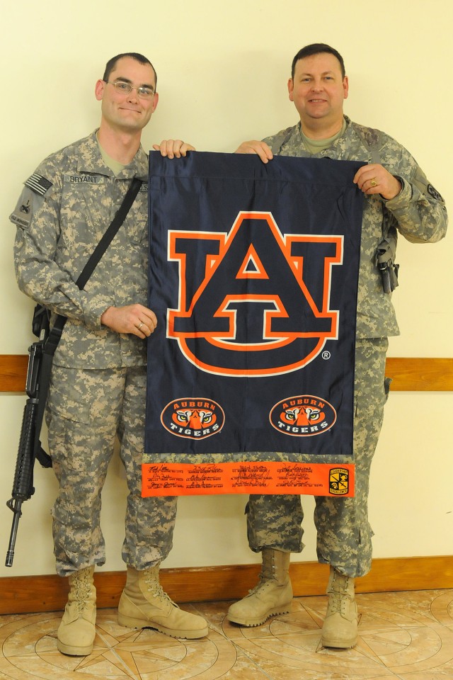 Sgt. Benjamin Bryant, a truck driver with the 40th Transportation Company, Special Troops Battalion, 15th Sustainment Brigade, and Col. Larry Phelps, the commander of the 15th Sustainment Brigade, pose with an Auburn University flag signed by...