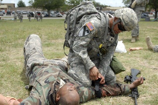 FORT HOOD, Texas - Spc. Christian Balas, from San Jose, Calif., places his knee above a tourniquet on the right arm of a "wounded" Soldier during Expert Field Medical Badge training, here, July 21. Balas serves as combat medic with Headquarters...
