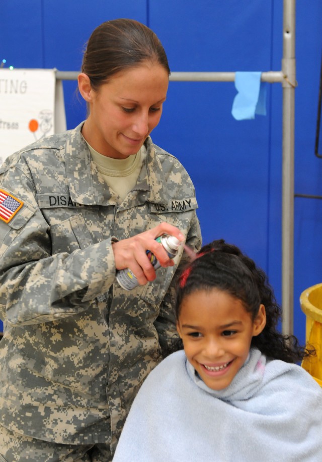 Sergeant Christina Disano, a driver with the 3d Sustainment Command (Expeditionary), sprays the hair of Taliyah Villanueva, 6, during the Pierce Elementary School Winter Festival Dec. 2. Disano was one of 25 Sustainer Soldiers who volunteered their t...