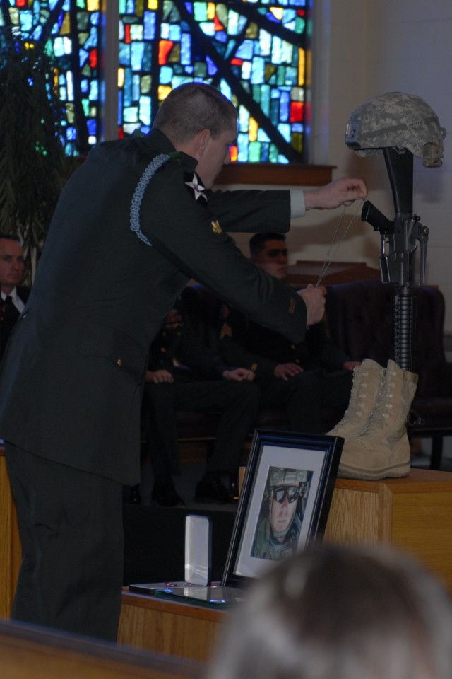 FORT HOOD, Texas - Spc. Ricky Scroggins, with 1st Battalion, 12th Cavalry Regiment, 3rd Brigade Combat Team, 1st Cavalry Division, places identification tags on the traditional display of boots, rifle and helmet at Staff. Sgt. Justin Tate's...
