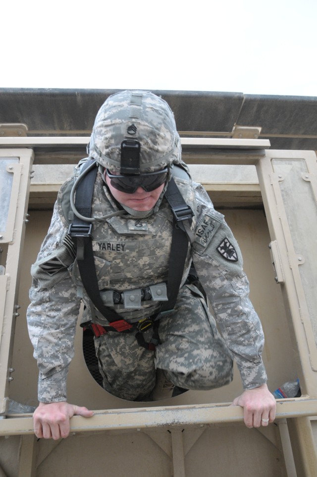 Staff Sgt. John Yarley, a 7th Sustainment Brigade information systems security Noncommissioned Officer, climbs out of the gunner hatch of a Mine Resistant Ambush Protected vehicle simulator Feb. 11 at Kandahar Airfield. Egress training for the...