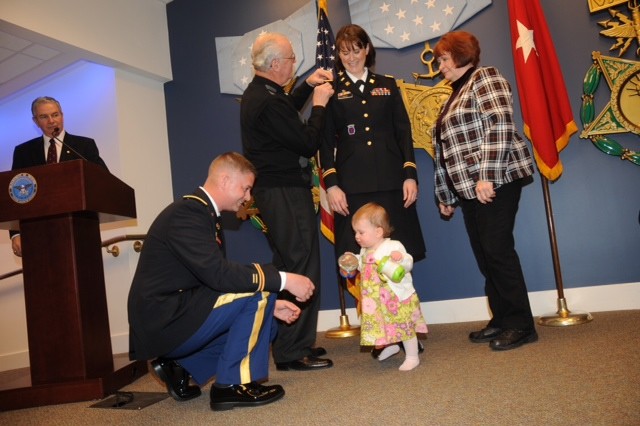 Lt. Col. Renee Mann is all smiles as her parents, Joseph Paulus and Shirley Miller, assist in placing on her new rank while newly promoted husband Lt. Col. Robert Mann shares a moment with their daughter Olivia.  The Manns were promoted in a joint ce...