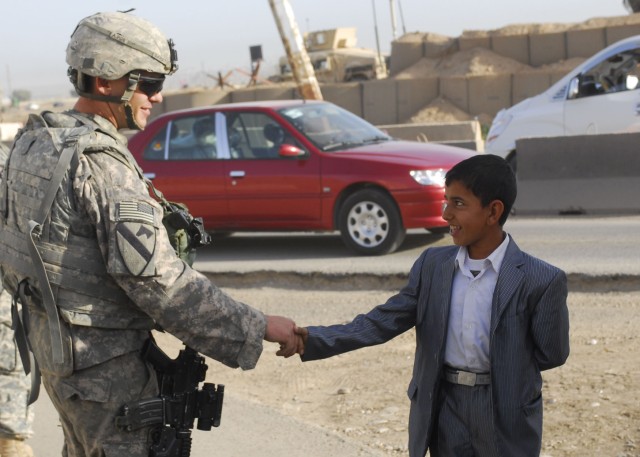 CONTINGENCY OPERATING SITE WARRIOR, Iraq - Spc. Shane Darst, an armor crewmember serving with Company D, 2nd Battalion, 12th Cavalry Regiment, attached to the 1st Advise and Assist Task Force, 1st Infantry Division, shakes hands with a young child...