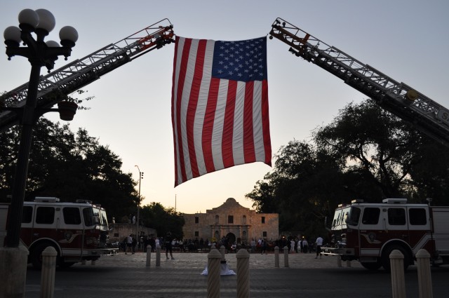 A flag draped between two SAFD firetrucks frames the facade of the Alamo at dawn Sept. 11.