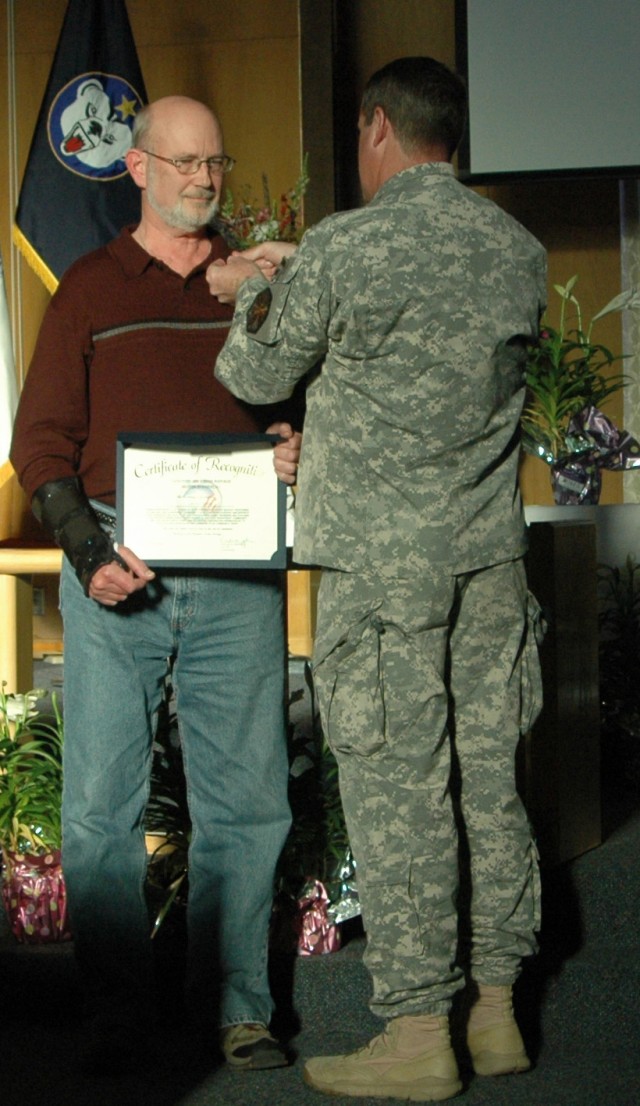 Charles Hamby, volunteer at Bassett Army Community Hospital receives a lapel pin from Col. Ronald M. Johnson, commander, United States Army Garrison Fort Wainwright during the Volunteer Recognition Ce