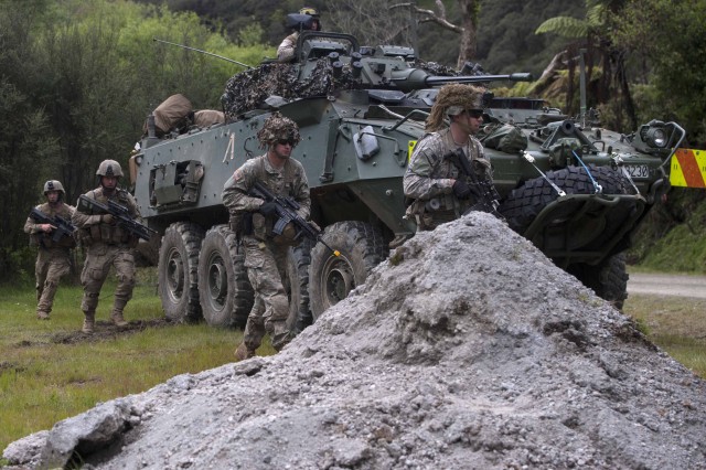 New Zealand and US Soldiers maneuver around light armored vehicle