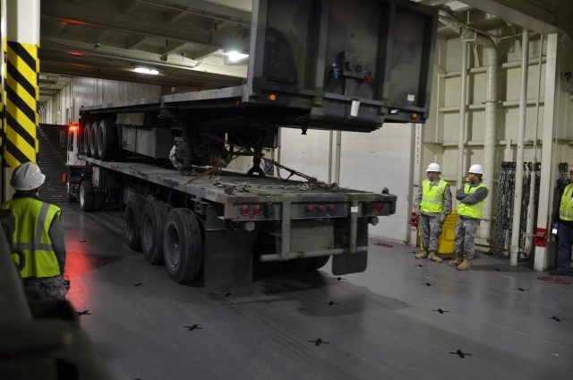 Truck with trailers backing down into the cargo hold of USNS Watkins.