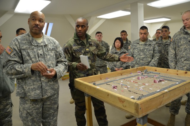 Sous-Lieutenant Fabrice Guy briefs the 557th ASMC, utilizing his sand table for orientation