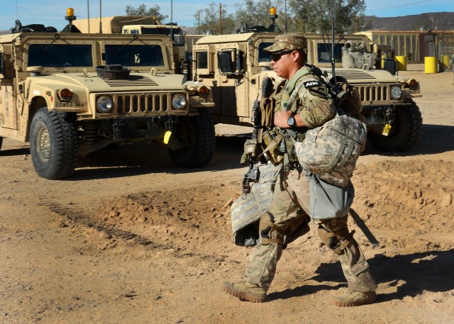 Sgt. Bryan Rodriguez walks with gear to M2 Bradley Fighting Vehicle