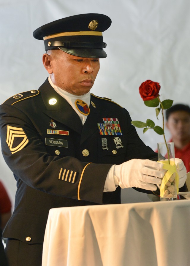 Sgt. 1st Class Allan Vergara places a yellow ribbon around a glass holding a rose at the missing man table
