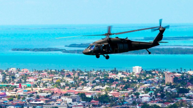 A UH-60 Blackhawk flies over Belize City while transporting Soldiers and Marines