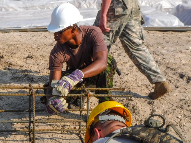 A soldier with the Belize Defense Force secures a chair to a rebar footer cage