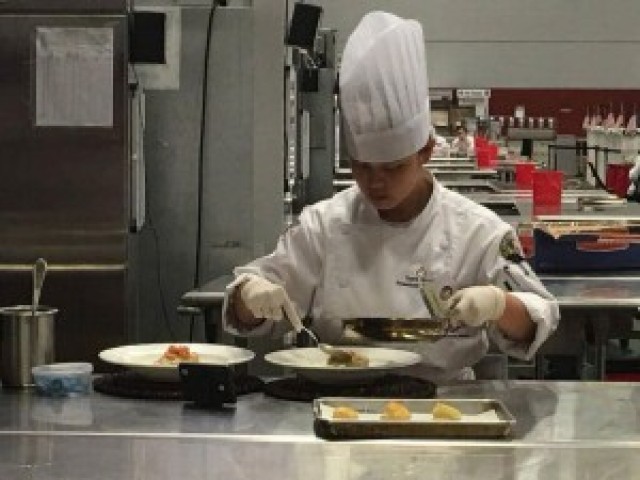 Spc. Anne Nicole Yapcengo, 307th Expeditionary Signal Battalion, focuses on preparing her main course for the judging event of the competition.