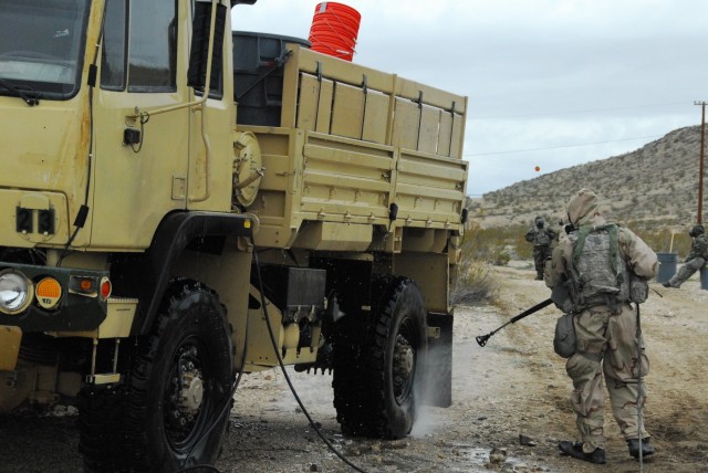 Soldier sprays water to decontaminate truck