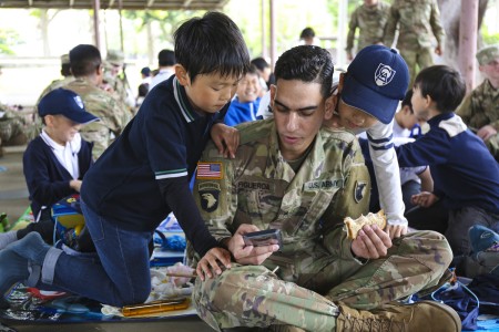 Sgt. Alexander Figueroa, assigned to the 38th Air Defense Artillery Brigade, shows LCA Kokusai Elementary School students a game on his cellphone while eating lunch during an Earth Day event April 24, 2019, at Sagami General Depot, Japan. (U.S. Army photo by Noriko Kudo)