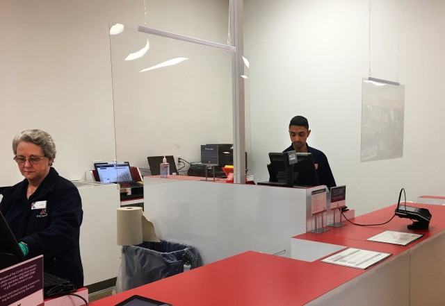 Linda Philpot (left) and Luis Lleras provide customer service behind the Plexiglas shields hanging from the ceiling. Members of the marketing team constructed the shields from existing materials and, with the help of maintenance staff, mounted...