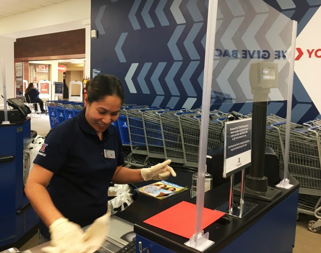 Edna Claycomb, a cashier at the Fort Knox Main Exchange, scans a product behind the protection of a Plexiglas shield. The shields have been installed at key AAFES locations since March 25, 2020, to help block the spread of COVID-19. (Photo...