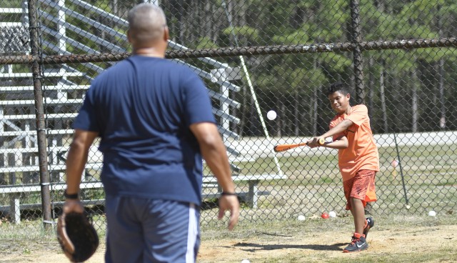 Zadkiel Agosto swings at a pitch thrown by his father, retired Sgt. 1st Class Rafael Agosto, during a practice session March 19 at the A Avenue baseball field.  Nine-year-old Zadkiel, a student at Prince George County’s Harrison Elementary School, has not had classes since March 16, when the county closed its schools due to coronavirus concerns.   While Zadkiel has kept busy with school take-home lessons, his father said he has been anxious to break his learning routine so the two took advantage of warm temperatures and an empty baseball field to play catch and hit some ball.  “I don’t want him close to that Playstation stuff,” said a chuckling SFC Agosto, noting he prefers some form of physical activity for his son. He also said parents need to be creative and resourceful in finding activities for children while school is suspended, and they should not hesitate to lean on one another to get by. “We’re Americans, we know how to overcome,” he said.