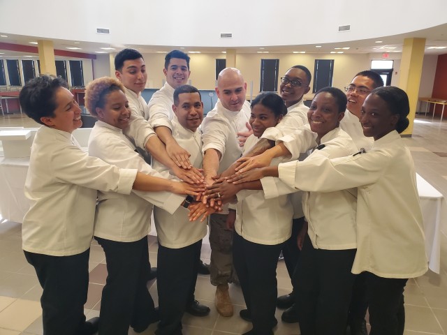 FORT BLISS, Texas - The Fort Bliss and 1st Armored Division Culinary Team, otherwise known as Team Tribute, stack their hands together in a show of solidarity at the Culinary Training Lab on Feb. 4. The culinary specialists competed at the 45th Annual Joint Culinary Training Exercise (JCTE) which took place from Mar. 4 - 13 at Fort Lee, Virginia. The JCTE is administered by the Joint Culinary Center of Excellence (JCCoE) and is the largest military cooking competition in North America sanctioned by the American Culinary Federation (ACF). (U.S. Army photo by Jean S. Han)