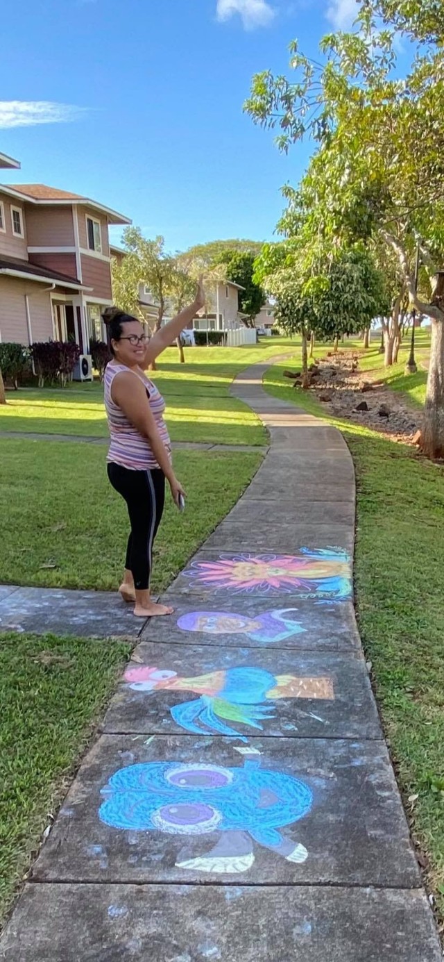 Diana Gibson poses with her artwork on Wheeler Army Airfield, Hawaii during the “Chalk the Walk” event which began March 21, 2020 on the island of Oahu. This event started as a way to spread some joy to others as they went for walks during the COVID-19 social distancing directive and has continued producing artwork more than a week after it began. (Photo courtesy of Diana Gibson)