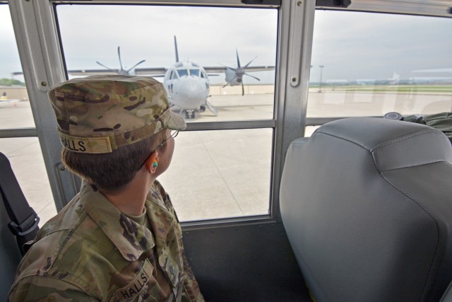 A Soldier looks out through a bus window to the C-27 aircraft that will fly her to her duty assignment. She and her fellow Soldiers were transported in controlled air and ground movements to their next duty of assignment as an exception to the Department of Defense stop movement enacted to stop the potential spread of the 2019 Coronavirus Disease, or COVID-19.