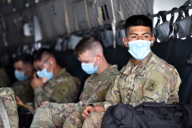 A Soldier looks out of the loading ramp of a C-27 aircraft while he and his fellow Soldiers wear face masks and maintain social distance. The Soldiers were transported in controlled air and ground movements to their next duty of assignment as an exception to the Department of Defense stop movement enacted to stop the potential spread of the 2019 Coronavirus Disease, or COVID-19.