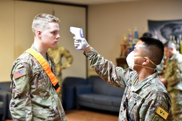 Spc. Justin Ocamop, a recently graduated 68W Combat Medic, checks the temperature of a fellow Combat Medic who is about to depart Fort Sam Houston, TX. The Soldiers were transported in controlled air and ground movements to their next duty of assignment as an exception to the Department of Defense stop movement enacted to stop the potential spread of the 2019 Coronavirus Disease, or COVID-19.