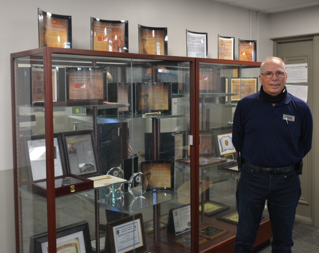 U.S. Army Garrison Fort Riley Safety Manager, Rick Hearron, stands in front of a display of national safety awards at Fort Riley, Kansas on April 13, 2020.