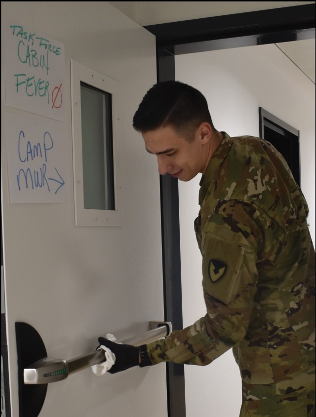 CHIÈVRES, Belgium – In this Army file photo, a member of Task Force Clean wipes a door down in the garrison headquarters. Task Force Clean is one of four task forces that protect the USAG Benelux community from the spread of COVID-19. (Courtesy...