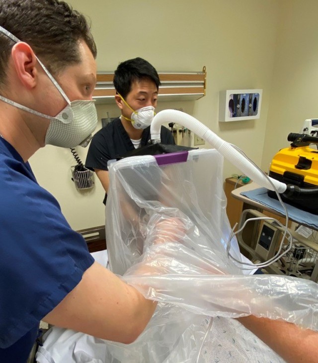 Dr. David Turer (left), and Dr. Jason Chang, both from the University of Pittsburgh Medical Center, perform an intubation procedure on a medical simulation mannequin using the new Individual Biocontainment Unit.