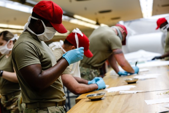 Pfc. James Hutchision, left, a parachute rigger with the 647th Quarter Master Company, 3rd Expeditionary Sustainment Command, prepares fabric to be sewn into protective masks at Fort Bragg, N.C., on April 15, as part of Operation Dragon Mask. Units from across Fort Bragg were repurposed to create face masks, face shields, and other personal protective equipment to be distributed as part of the COVID-19 response. (U.S. Army Photo by Spc. Hubert D. Delany III)