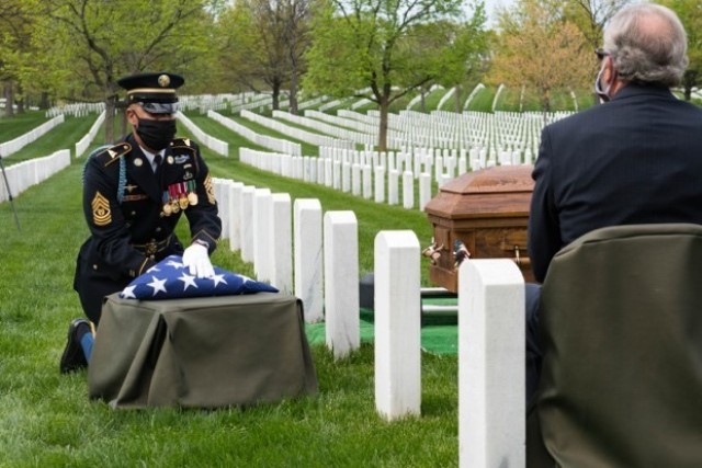 Command Sgt. Maj. Robert Carter kneels to render final military honors while presenting the U.S. flag to the family of U.S. Army Retired Command Sgt. Maj. Robert M. Belch in Section 68 of Arlington National Cemetery, Arlington, Virginia, April 14, 2020. Carter placed the U.S. flag on a small box to maintain the 6-foot social distancing guidelines.