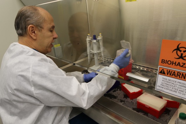 Emerito Rodriguez, medical technologist/biosafety officer, conducts the test in BSL3 and shows results on computer screen. Rodriguez batches samples for testing on a testing plate. (U.S. Army Courtesy photo by: Amabilia Payen, WBAMC Public Affairs.)