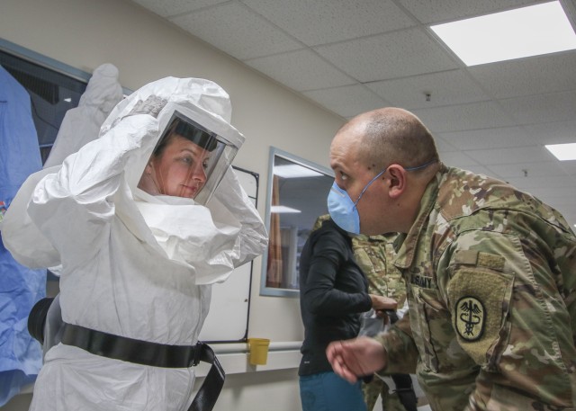 U.S. Army Sgt. Ryan Aker (right), a licensed practical nurse with the Medical-Surgical Unit at Landstuhl Regional Medical Center, assists U.S. Air Force Maj. April Oliver, assistant officer in charge, Intensive Care Unit, LRMC, with donning the...