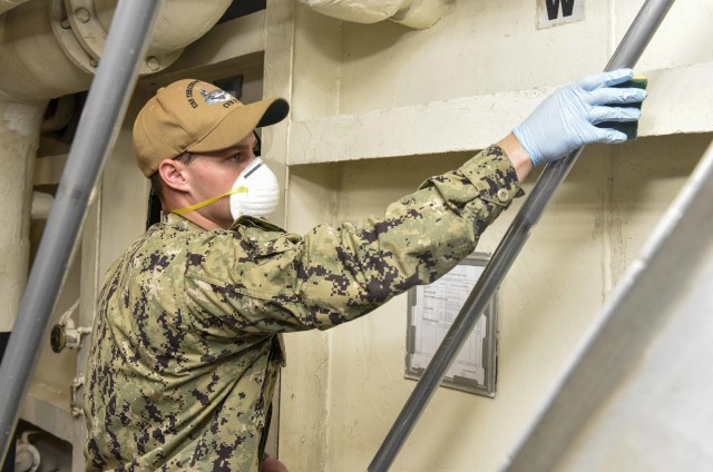 200419-N-FZ335-1025 APRA, Guam (April 19, 2020) U.S. Navy Aviation Structural Mechanic Airman Preston Rosiere, from Wichita, Kan., sanitizes a hand rail aboard the aircraft carrier USS Theodore Roosevelt (CVN 71) April 19, 2020. Upon arriving in...