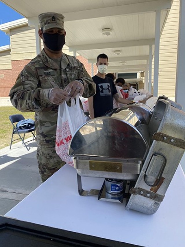 Staff Sgt. Josua Garo, 369th Composite Truck Company, Special Troops Battalion, 3rd Infantry Division Sustainment Brigade, hands off a bagged lunch to a Diamond Elementary School food service staff member April 29 on Fort Stewart. Garo is a volunteer for the  DoDEA Fort Stewart School Meal Program during the COVID-19 pandemic. He and nine other Soldiers are volunteering across post, helping to provide services to the community.