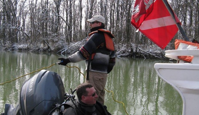 A dive tender maintains tension on a communication line during a mussel survey conducted in mid-winter.  A standby diver waits in the foreground.  Project schedules require diving during all seasons.