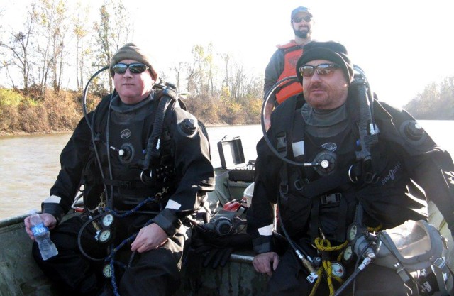 Dive team members travel to a new mussel survey location. Using smaller boats allows divers to access sites that may be upstream of blockages.  Divers are using dry suits and face masks during this operation.