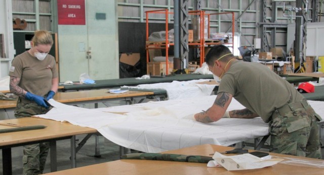 Spc. Kylie Nielsen (left) and Spc. Ernie Ramirez, parachute riggers from the 4th Quartermaster Theater Aerial Delivery Company, measure and cut out templates during the assembly process to produce face masks for U.S. Army Japan. (Photo by Chief Warrant Officer 4 Brian Perinon, Japan Support Team, AFSBn-NEA)